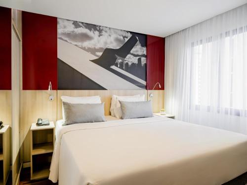 a bedroom with a large white bed and a painting at Mercure Sao Paulo Moema Times Square in Sao Paulo