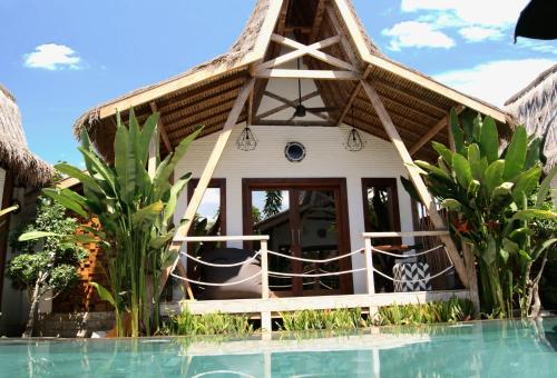 a house with a thatched roof next to a swimming pool at Kaleydo Villas in Gili Trawangan