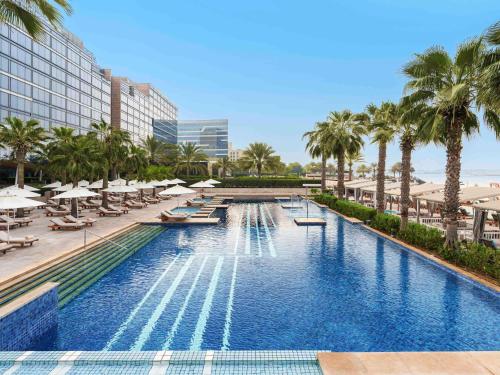 a swimming pool with lounge chairs and palm trees at Fairmont Bab Al Bahr in Abu Dhabi