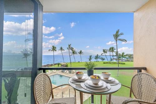 a table with two cups of coffee on a balcony with the ocean at Kihei Surfside 306 · KSS 306 Updated BeachFront 1BD w Ocean View in Wailea