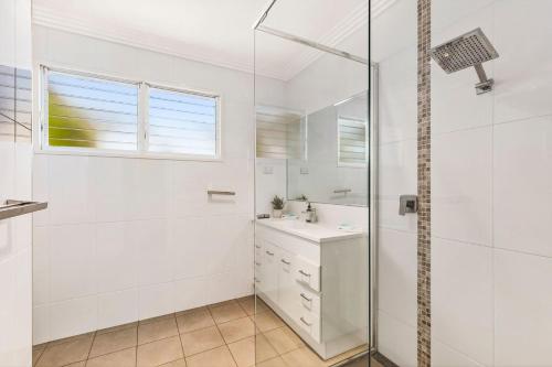 a white bathroom with a shower and a sink at Headland Beauty. in Urunga