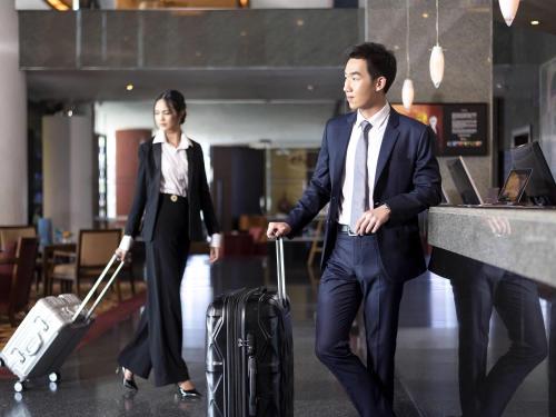 un hombre y una mujer caminando con equipaje en un aeropuerto en Novotel Bangkok Bangna, en Bangna