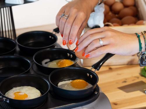 a woman cooking eggs in black pans on a stove at Mercure Bordeaux Chateau Chartrons in Bordeaux