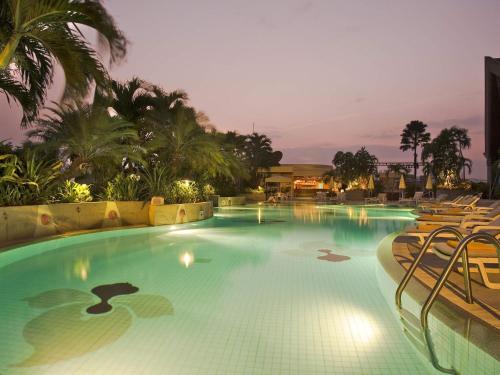 a swimming pool at night with chairs and palm trees at The Heritage Grand Khon Kaen Hotel and Convention in Khon Kaen