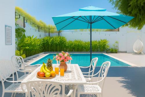 Una mesa con fruta y una sombrilla junto a una piscina. en Amory Villa Mui Ne, en Mui Ne