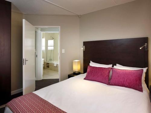 a bedroom with a large white bed with pink pillows at Mercure Hotel Bedfordview in Johannesburg