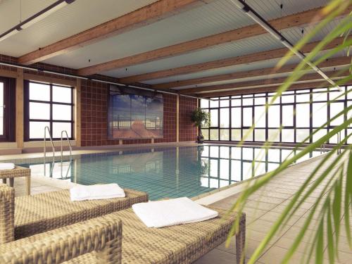 a swimming pool with two chairs in a building at Mercure Hotel am Messeplatz Offenburg in Offenburg