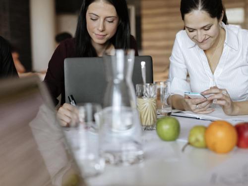 dos mujeres sentadas en una mesa mirando un celular en Mercure Hotel am Messeplatz Offenburg, en Offenburg