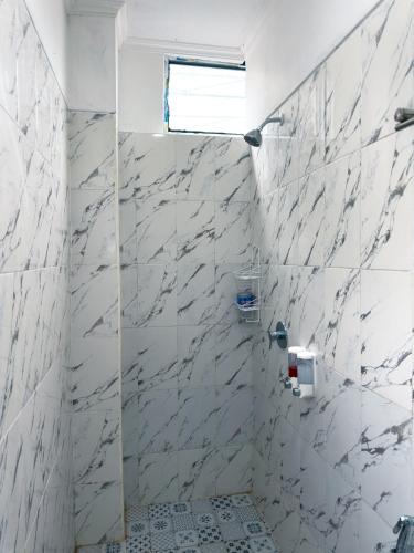 a bathroom with white marble walls and a shower at Dong Paloh Hostel in Munduk