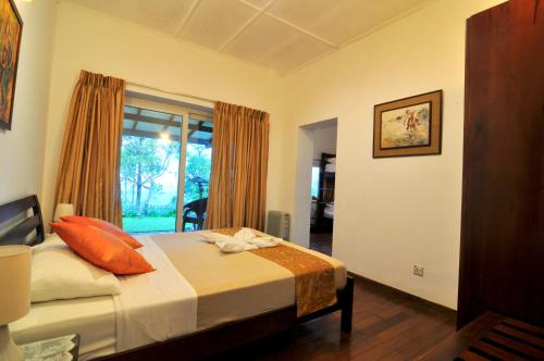 ein Schlafzimmer mit einem Bett mit orangefarbenen Kissen und einem Fenster in der Unterkunft Clouds Holiday Bungalow in Haputale