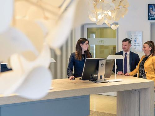 a group of people standing around a desk with a computer at Mercure Hotel Hannover Mitte in Hannover