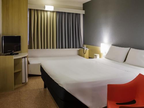 Una habitación de hotel con una cama grande y una silla roja. en ibis Araçatuba, en Araçatuba