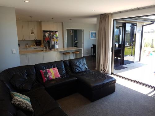 a living room with a black leather couch and a kitchen at Beach days and cozy stays - sleeps seven in Tauranga