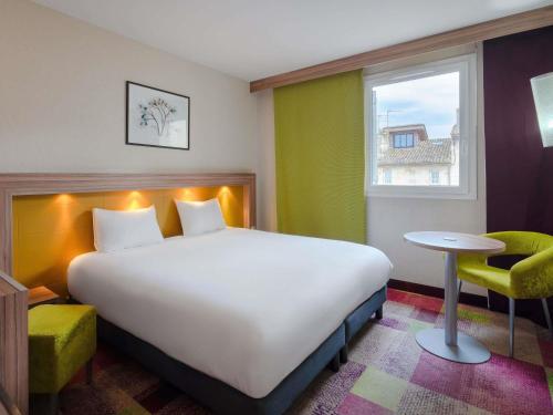 a bedroom with a large bed and a table and a window at Mercure Libourne Saint Emilion in Libourne