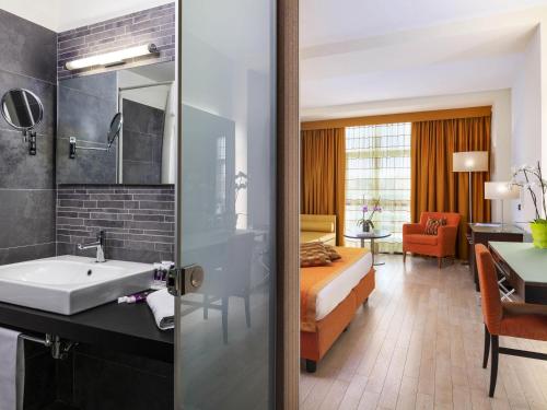 a bathroom with a bed and a sink in a room at Hotel Mercure Siracusa in Siracusa