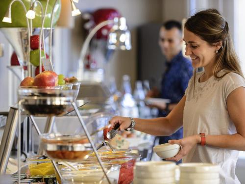 Una mujer parada en una cocina preparando comida. en Mercure Thalasso & Spa Port Fréjus, en Fréjus
