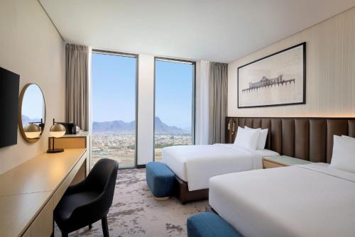 a hotel room with two beds and a desk at Doubletree by Hilton Madinah Gate in Al ‘Awālī