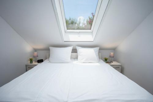 a bedroom with a white bed with a window at Grashaus Groothusen in Krummhörn