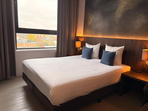 a bedroom with a bed with blue pillows and a window at Hotel Elisabeth in Mechelen