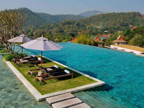 a pool with chairs and umbrellas next to a mountain at Veranda High Resort Chiang Mai - MGallery Collection, Accor Hotel in Hang Dong