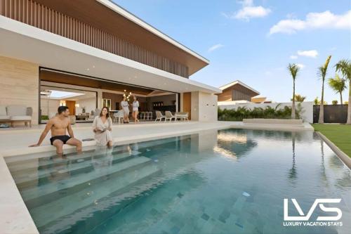 two people sitting on the edge of a swimming pool in a house at Zen Oasis Villa at Casa de Campo in La Romana
