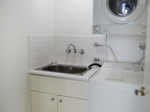 Una pequeña cocina con fregadero y lavadora. en The Sebel Quay West Auckland, en Auckland
