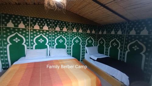 a bedroom with two beds and a green wall at Family Berber Camp in Merzouga