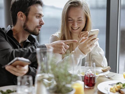 um homem e uma mulher sentados à mesa olhando para o celular em Mercure Hotel Koeln Belfortstrasse em Colónia
