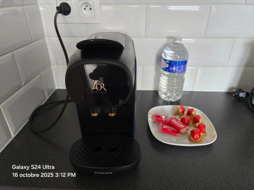 a coffee maker with a bowl of fruit and a bottle of water at Giena - SILS in Caen