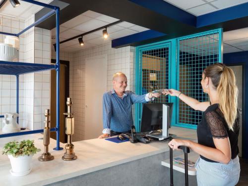a man and a woman shaking hands at a counter at ibis budget Pertuis Portes du Luberon in Pertuis