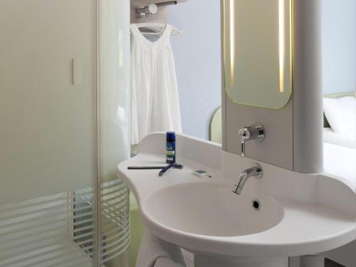 Un baño blanco con lavabo y espejo. en ibis budget Montceau les Mines, en Montceau-les-Mines