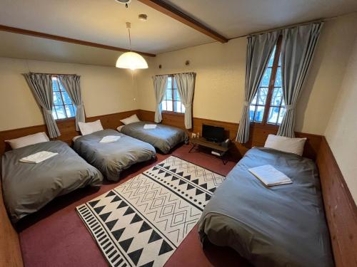 a room with three beds and a tv and windows at Shika Lodge in Iiyama