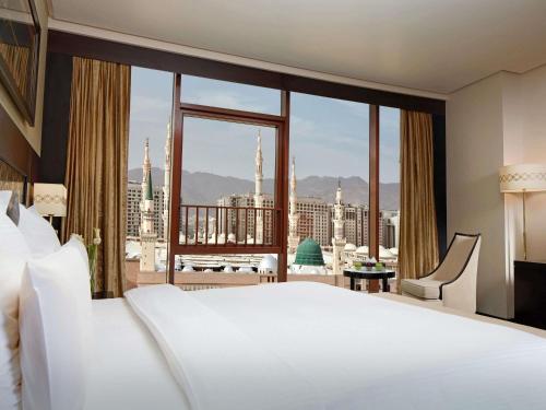 a bedroom with a large white bed and a large window at Zamzam Pullman Madina in Al Madinah