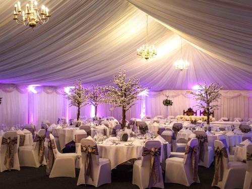 a marquee with white tables and chairs and purple lighting at Mercure Haydock Hotel in Haydock
