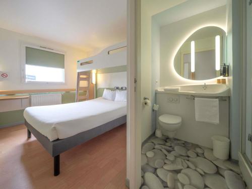 a bedroom with a bed and a sink and a mirror at Ibis Budget Sarrebourg Buhl in Sarrebourg