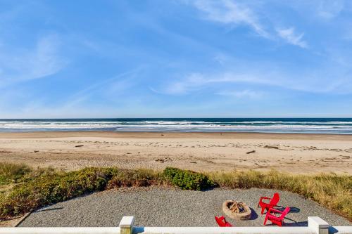 a beach with two red beach chairs and the ocean at Oceanfront home with a washer dryer and beach access in Rockaway Beach
