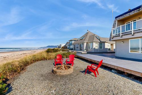 two red chairs and a fire pit on a beach at Oceanfront home with a washer dryer and beach access in Rockaway Beach