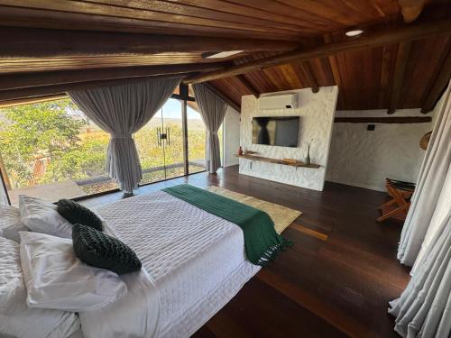 a bedroom with a large bed and a large window at Vila Kairós - 1 Cabana privativa com banheira e 2 suítes independentes - Vista Incrível Cozinha Gourmet Fogueira in Alto Paraíso de Goiás