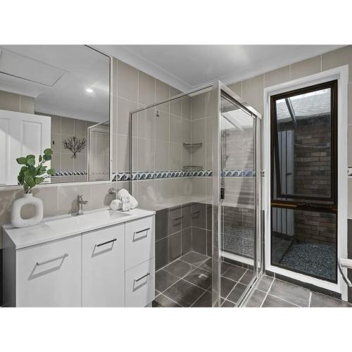 a white bathroom with a shower and a sink at Spacious Family Retreat in Perfect Location! in Brisbane