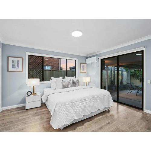 a white bedroom with a large bed and sliding glass doors at Spacious Family Retreat in Perfect Location! in Brisbane