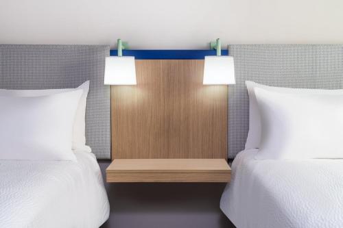 two beds with white pillows and a table between them at Garner Hotel Glen Burnie BWI Airport Area by IHG in Glen Burnie