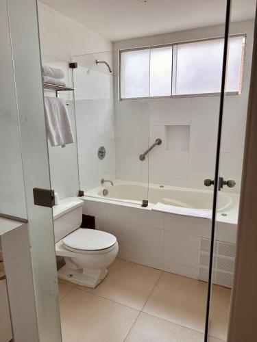 a white bathroom with a toilet and a bath tub at El Golf Hotel Boutique in Lima
