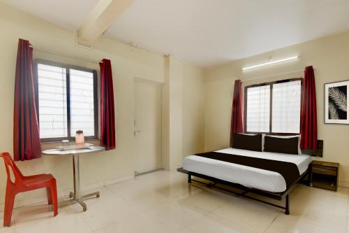 a bedroom with a bed and a table and two windows at Hotel O Prarambh inn in Pune