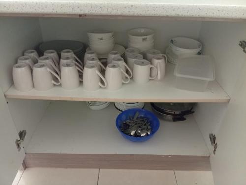 a shelf filled with white cups and a blue bowl at Marina Island Seafront Villa by Monte Villas in Lumut