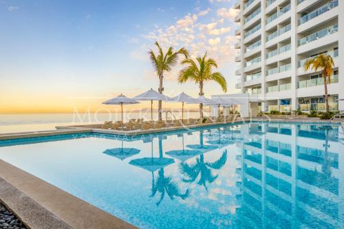 a pool with chairs and umbrellas in front of a building at Harbor 12005 Huge unit 2 Balconies Beachfront by Moikkarentals in Puerto Vallarta
