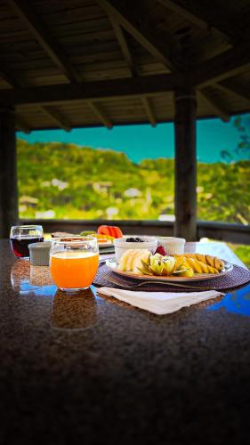una mesa con un plato de comida y un vaso de jugo de naranja en Pousada Minha Rosa Paixão - PRAIA DO ROSA, SC, en Imbituba