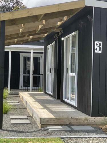 une maison noire avec une terrasse couverte et une terrasse en bois dans l'établissement Hosts on the Coast Pawprint Cabins, à Whitianga