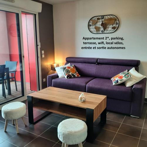 a living room with a purple couch and a coffee table at Patio Arena, appartement 2 étoiles, terrasse, parking, wifi, entrée et sortie autonomes, local vélos in Bayonne