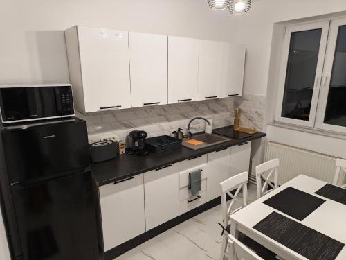 a kitchen with white cabinets and a black refrigerator at Terra Ștrand Residence Ștei in Ştei