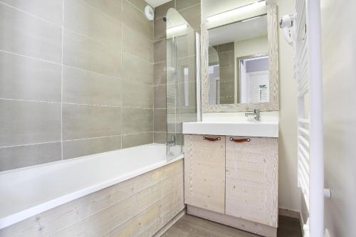 une salle de bain avec une baignoire, un lavabo et un miroir dans l'établissement Résidence Odalys Le Panoramic, à Flaine